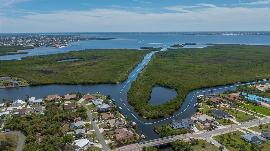 An aerial view shows a canal winding through mangroves toward a large open bay — 18546 ASHCROFT CIRCLE, PORT CHARLOTTE, FL