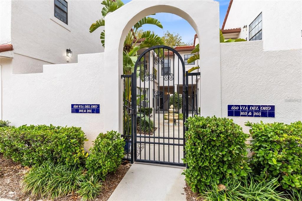 A black wrought iron gate sits within a white arched entryway leading to a courtyard — 550 VIA DEL ORO DRIVE UNIT 102, ALTAMONTE SPRINGS, FL
