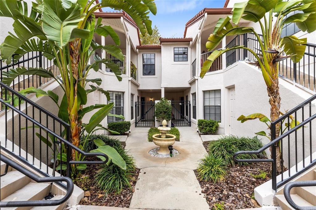 A courtyard with a central fountain, stairs, and palm trees between two residential buildings — 550 VIA DEL ORO DRIVE UNIT 102, ALTAMONTE SPRINGS, FL