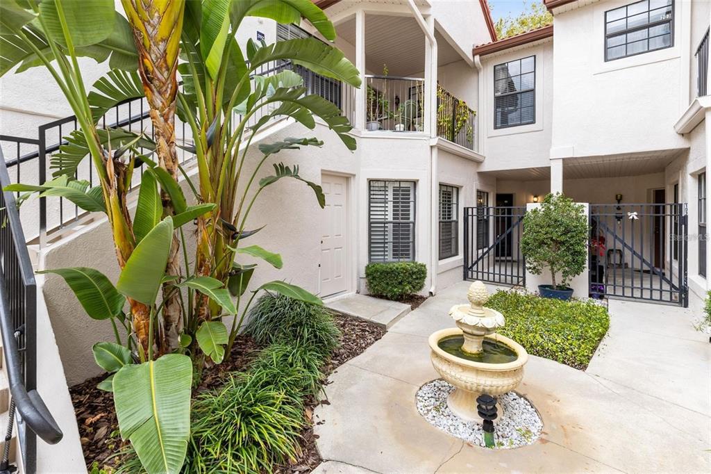 A courtyard features a stone fountain, lush landscaping, and a staircase leading to an upper balcony — 550 VIA DEL ORO DRIVE UNIT 102, ALTAMONTE SPRINGS, FL