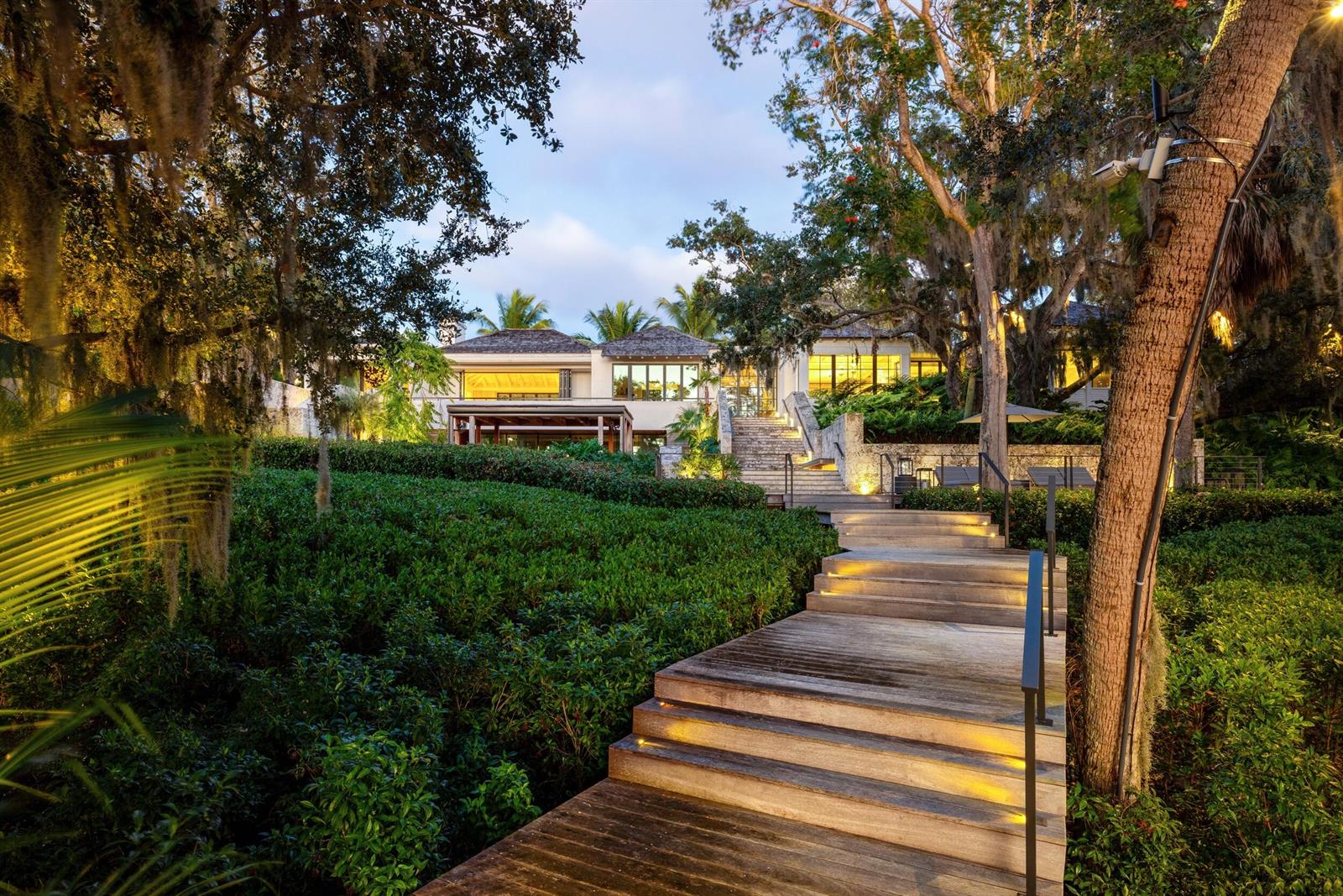 A wooden staircase leads through lush landscaping toward a multi-story house at twilight — 109 S River Road, Sewalls Point FL 34996, SEWALLS POINT, FL