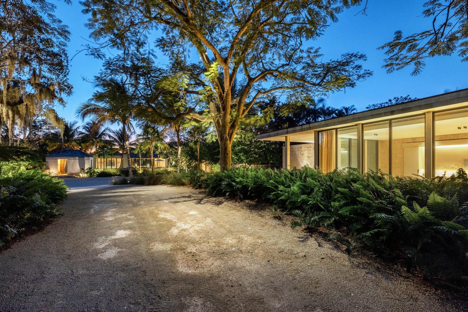 A gravel driveway leads to a modern home with floor-to-ceiling windows and lush landscaping — 109 S River Road, Sewalls Point FL 34996, SEWALLS POINT, FL