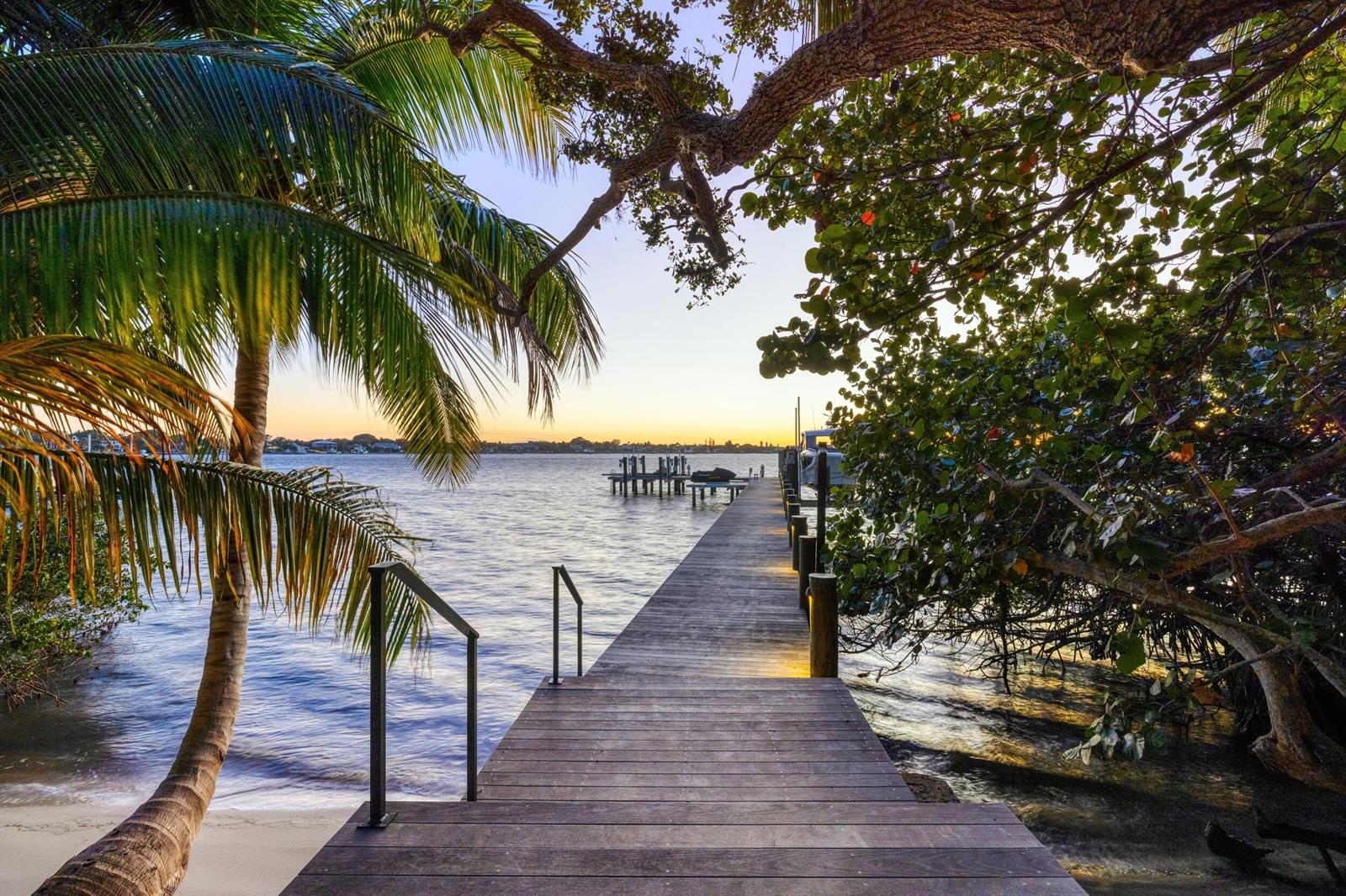 A wooden dock extends over the water toward a sunset view framed by tropical trees — 109 S River Road, Sewalls Point FL 34996, SEWALLS POINT, FL