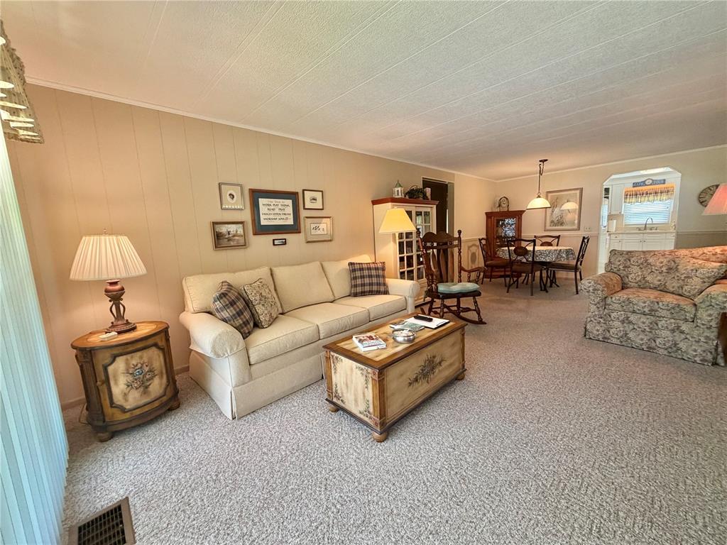 A living room with beige walls, carpeted floors, a sofa, coffee table, and dining area — 146 HIBISCUS WAY, LEESBURG, FL