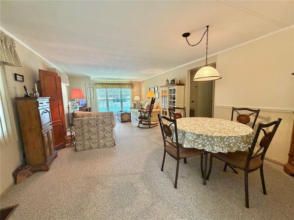 A carpeted living and dining area features a round table, upholstered furniture, and large windows — 146 HIBISCUS WAY, LEESBURG, FL