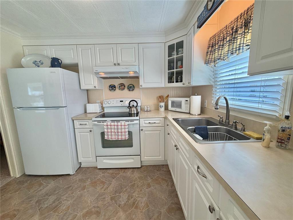 A kitchen features white cabinets, white appliances, a double sink, and patterned vinyl flooring — 146 HIBISCUS WAY, LEESBURG, FL