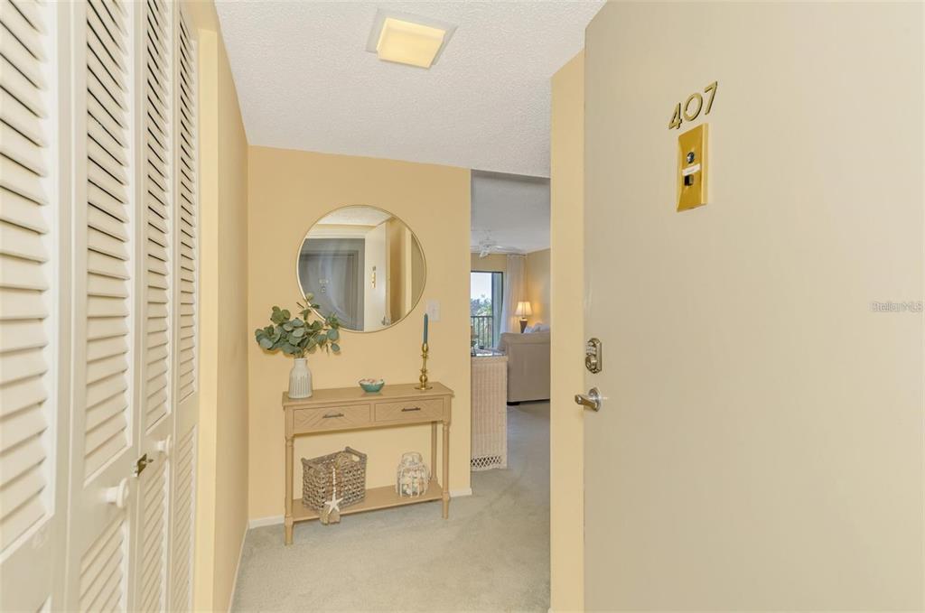 An entryway with a console table, round mirror, and a door labeled 407 — 6114 43RD STREET W UNIT 407E, BRADENTON, FL