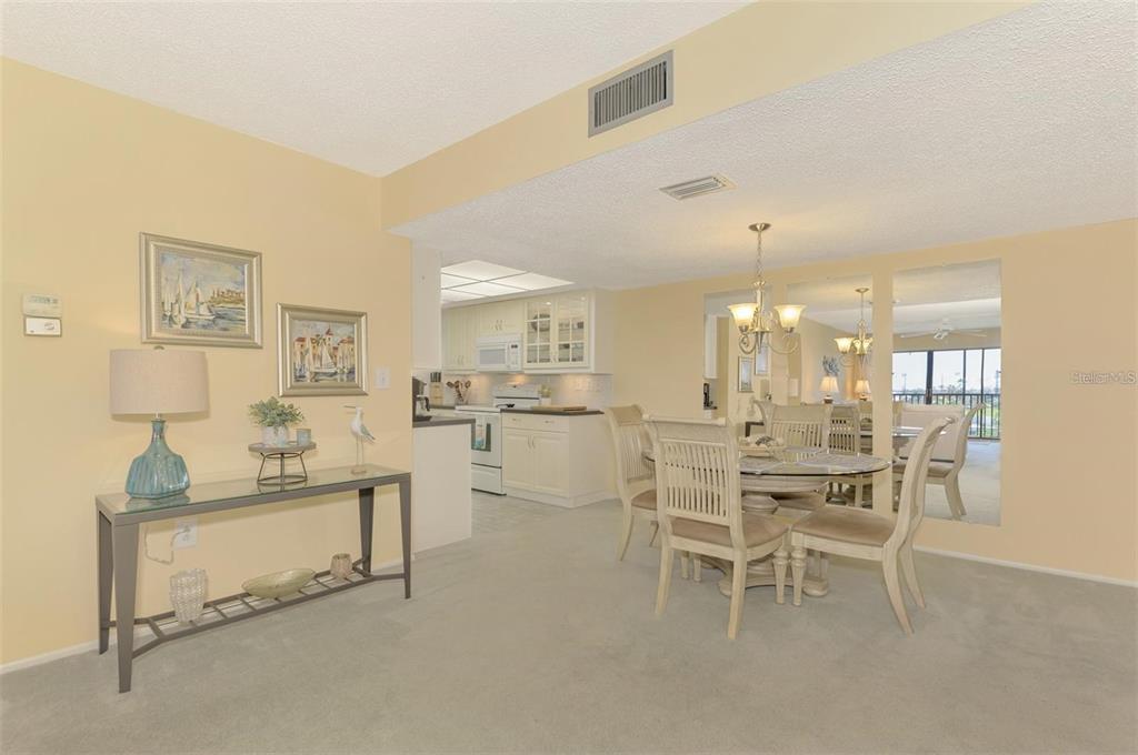 A dining area with a glass-topped table and chairs sits adjacent to a white kitchen — 6114 43RD STREET W UNIT 407E, BRADENTON, FL