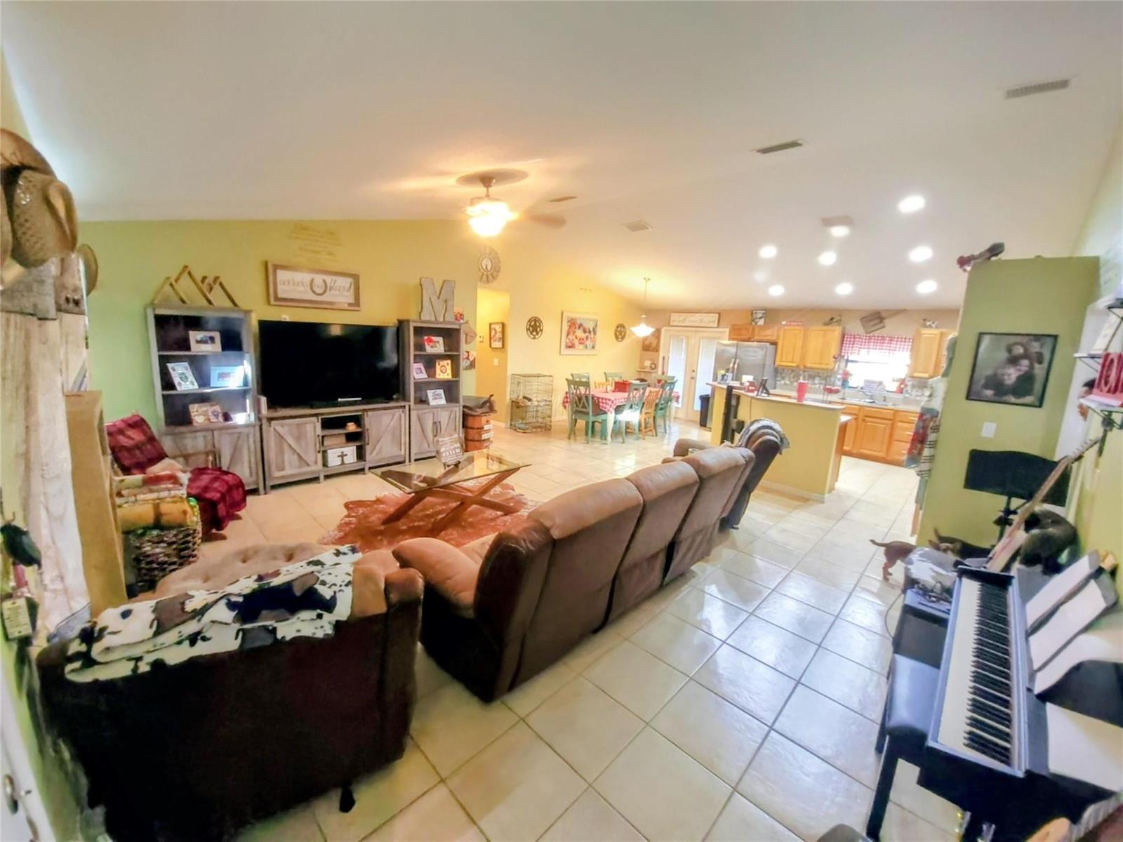 An open-concept living room and kitchen featuring tile flooring, a brown sectional, and wooden cabinetry — 1153 Jerdik Drive, Moore Haven FL 33471, MOORE HAVEN, FL
