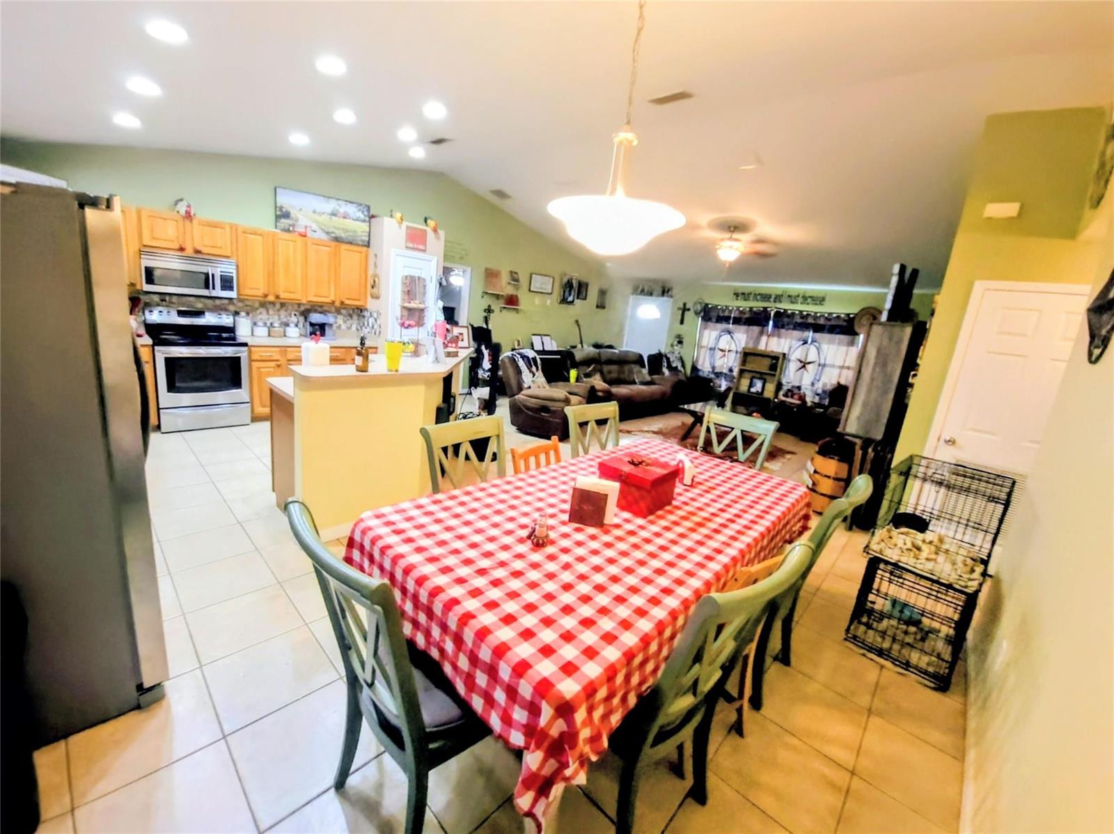 A dining area with a red checkered tablecloth sits adjacent to an open-concept kitchen — 1153 Jerdik Drive, Moore Haven FL 33471, MOORE HAVEN, FL