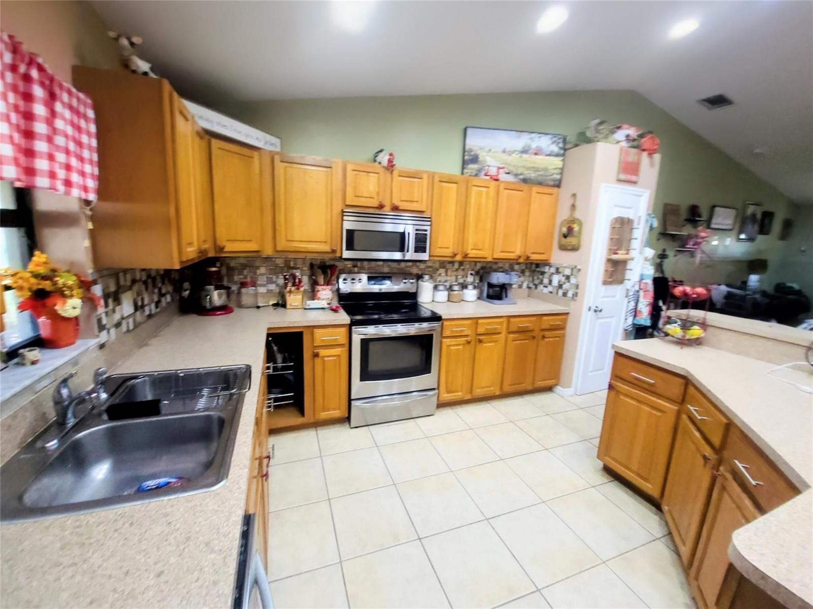A kitchen features light wood cabinets, stainless steel appliances, and beige tile flooring — 1153 Jerdik Drive, Moore Haven FL 33471, MOORE HAVEN, FL