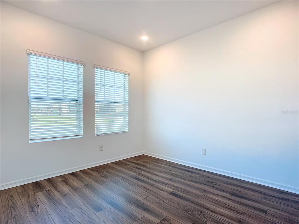 An empty room with white walls, two windows with blinds, and dark wood-look flooring — 1469 ARBOR HILL DRIVE, DELTONA, FL