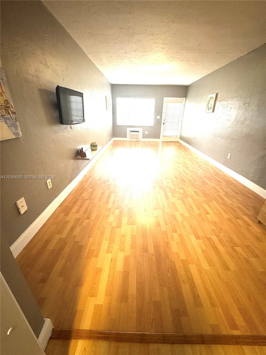 A long, narrow living room features gray walls, light wood flooring, and a wall-mounted television — 1611 West Ave # 10, Miami Beach FL 33139, MIAMI BEACH, FL