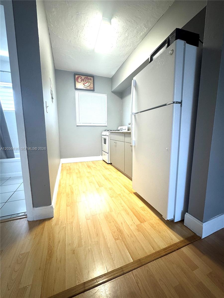 A narrow kitchen features light wood flooring, gray walls, a white refrigerator, and a stove — 1611 West Ave # 10, Miami Beach FL 33139, MIAMI BEACH, FL