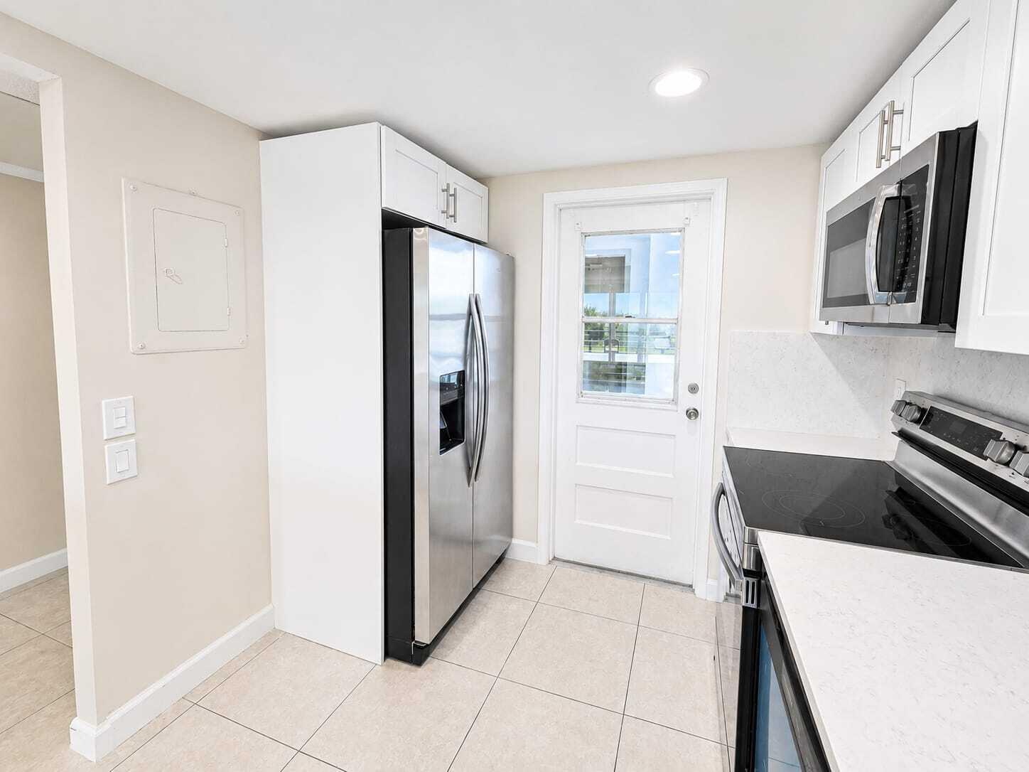 A kitchen features white cabinets, stainless steel appliances, a glass-paneled door, and light tile flooring — 2681 S Course Drive # 301, Pompano Beach FL 33069, POMPANO BEACH, FL