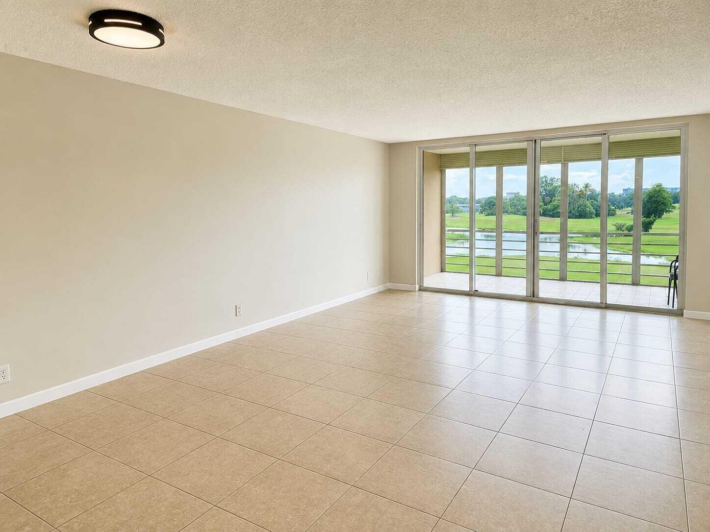 An empty living room with beige tile floors, a ceiling light, and sliding glass balcony doors — 2681 S Course Drive # 301, Pompano Beach FL 33069, POMPANO BEACH, FL