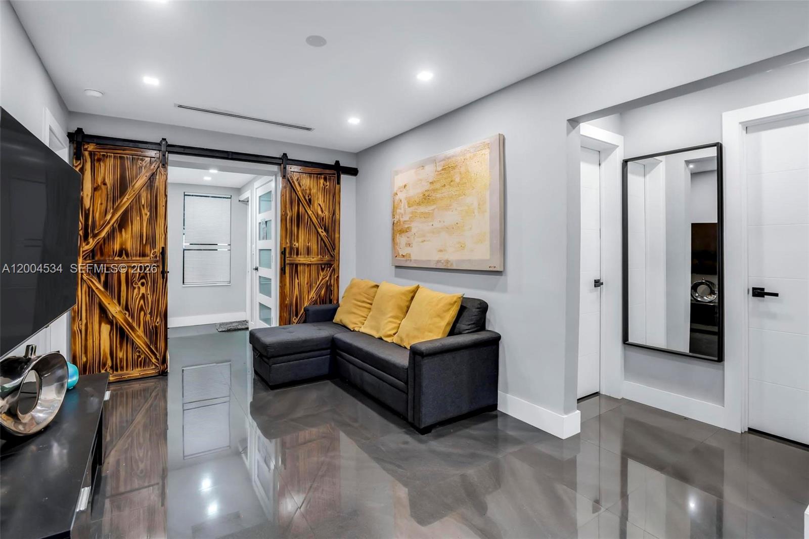 A living room features a dark gray sectional sofa, barn doors, and glossy tile flooring — 1741 NW 44th St, Miami FL 33142, MIAMI, FL