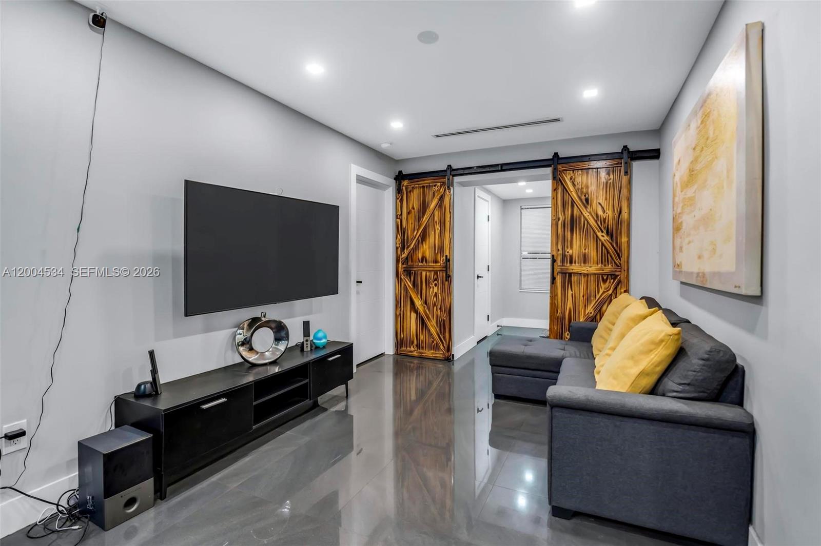 A living room features a wall-mounted television, a dark media console, and rustic sliding barn doors — 1741 NW 44th St, Miami FL 33142, MIAMI, FL