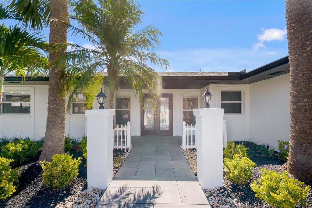 A paved walkway leads to the double front doors of a white house with palm trees — 3924 VERSAILLES DRIVE, TAMPA, FL
