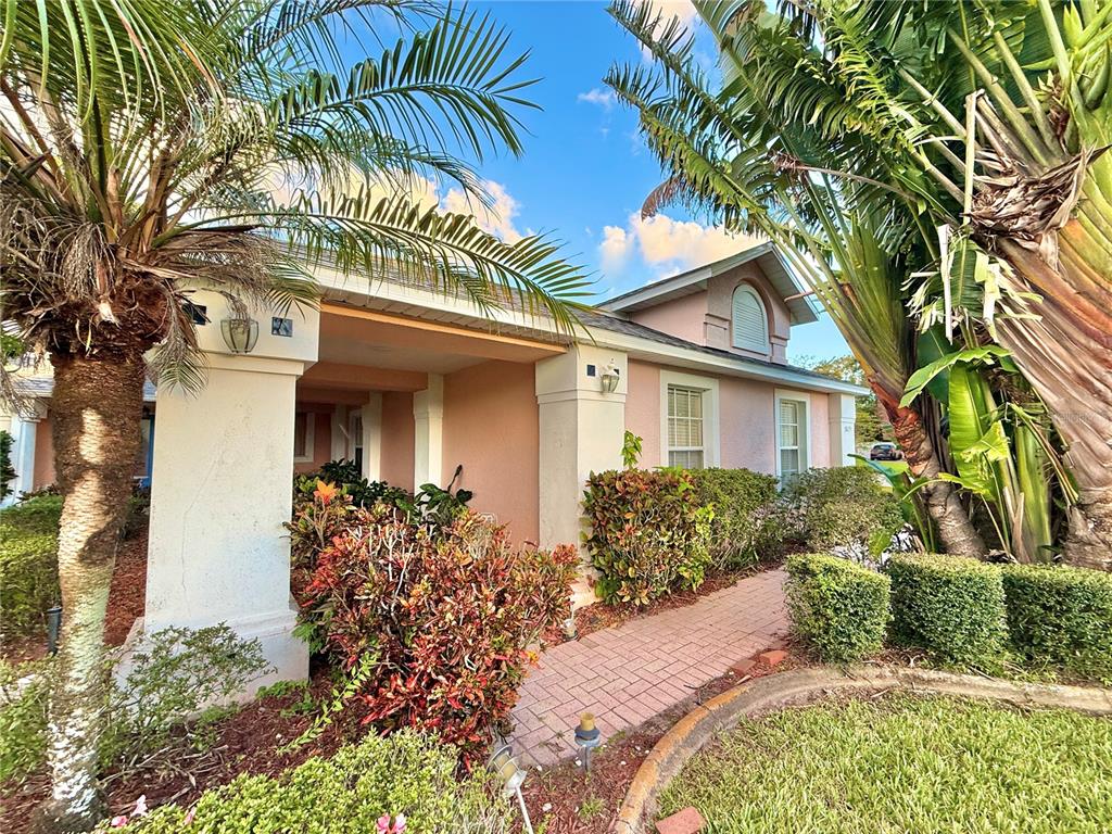A pink house exterior features a brick walkway, palm trees, and a covered entryway — 5829 GUENEVERE COURT, ST CLOUD, FL
