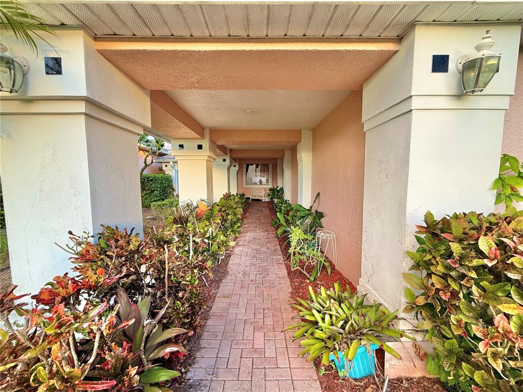 A brick walkway leads through a covered outdoor corridor lined with potted plants and shrubs — 5829 GUENEVERE COURT, ST CLOUD, FL