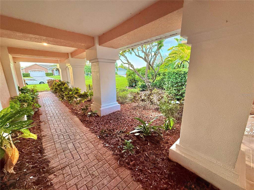 A covered brick walkway leads past white columns toward a landscaped yard and driveway — 5829 GUENEVERE COURT, ST CLOUD, FL