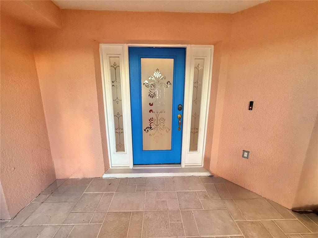 A bright blue front door with decorative glass panels sits within a peach-colored entryway — 5829 GUENEVERE COURT, ST CLOUD, FL