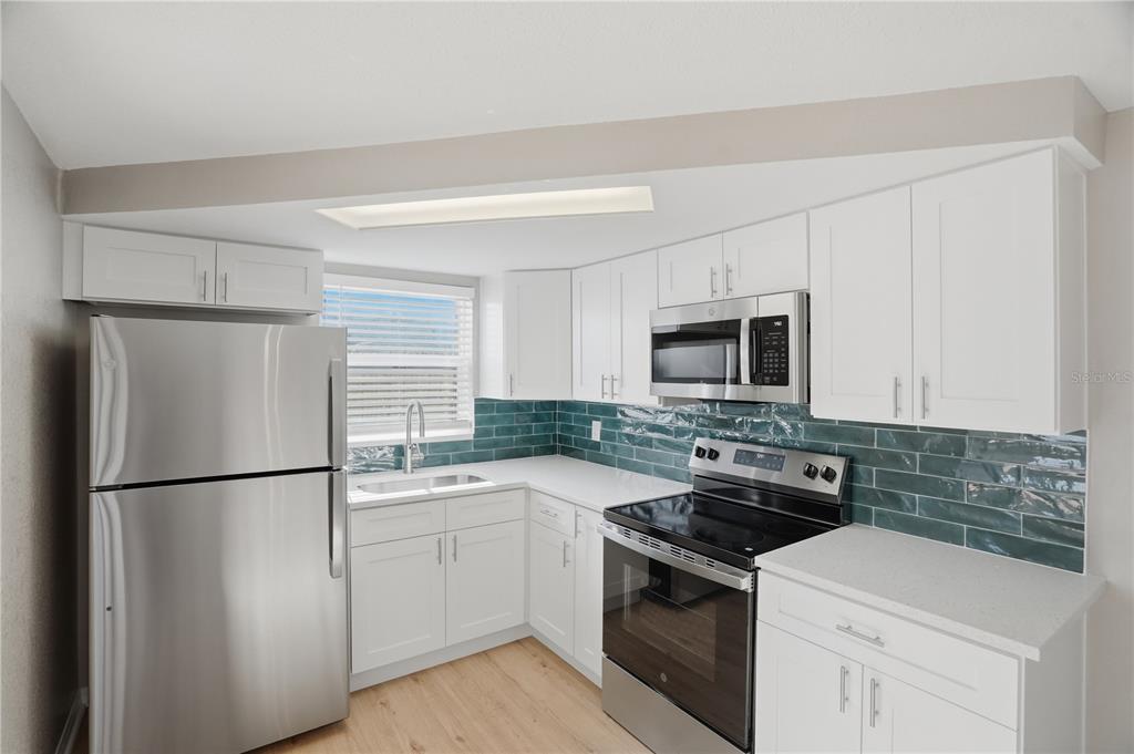 A kitchen with white cabinets, stainless steel appliances, and a teal subway tile backsplash — 3104 SALISBURY DRIVE, HOLIDAY, FL