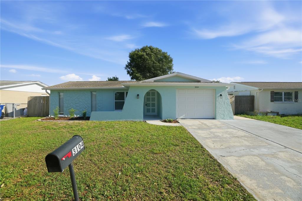 A light green single-story house with a white garage door and a front-facing mailbox — 3104 SALISBURY DRIVE, HOLIDAY, FL
