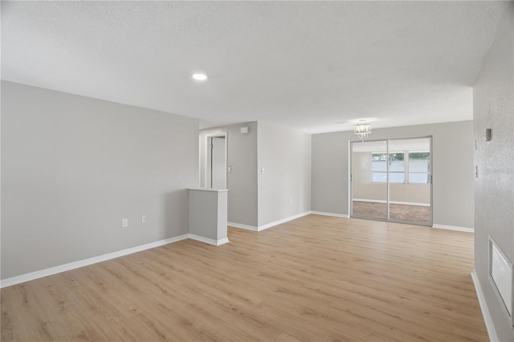 An empty living room features light wood-look flooring, gray walls, and sliding glass patio doors — 3104 SALISBURY DRIVE, HOLIDAY, FL