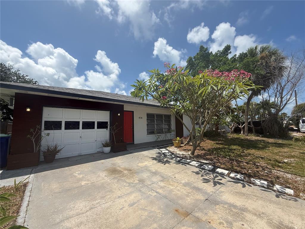 A single-story house with a white garage door, red front door, and a flowering tree — 414 86TH AVENUE, ST PETE BEACH, FL