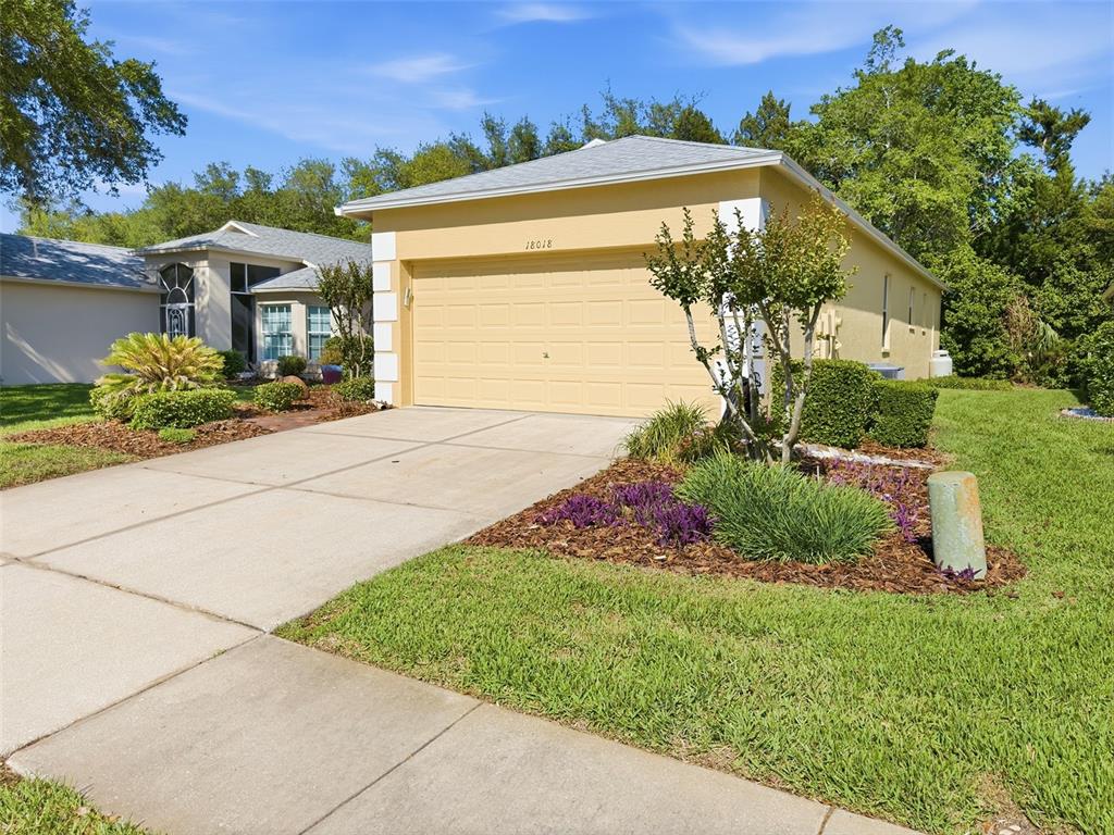 A yellow house with a two-car garage and a concrete driveway sits on a lawn — 18018 WEBSTER GROVE DRIVE, HUDSON, FL
