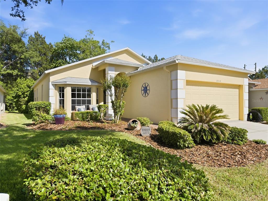 A single-story yellow house with a two-car garage and a front bay window — 18018 WEBSTER GROVE DRIVE, HUDSON, FL