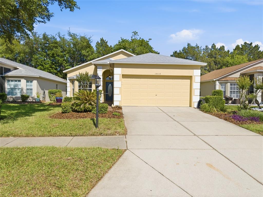 A single-story house with a yellow exterior, a two-car garage, and a concrete driveway — 18018 WEBSTER GROVE DRIVE, HUDSON, FL