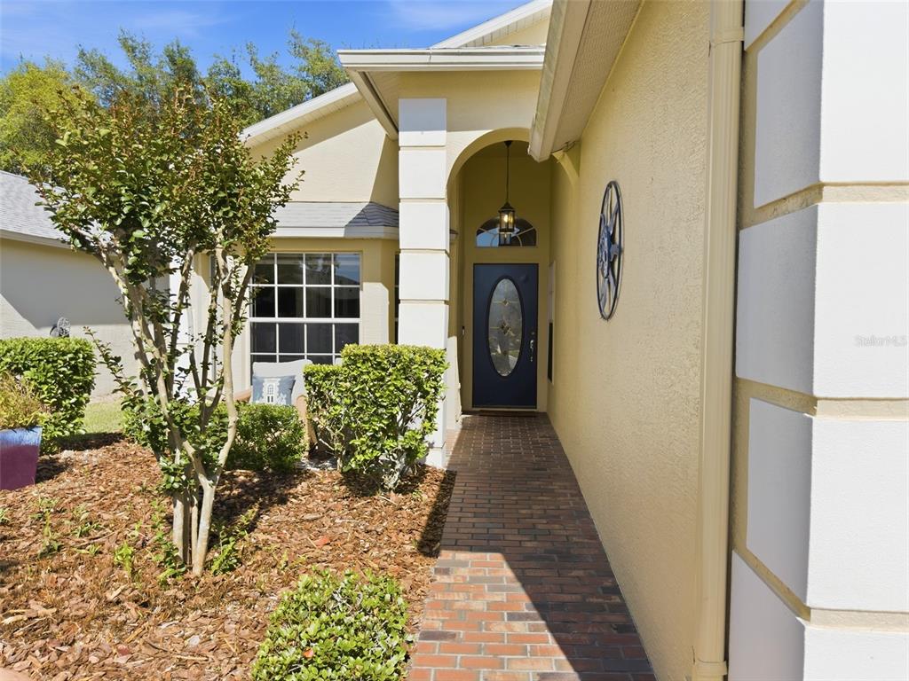 A brick walkway leads to the front entrance of a house with yellow stucco walls — 18018 WEBSTER GROVE DRIVE, HUDSON, FL