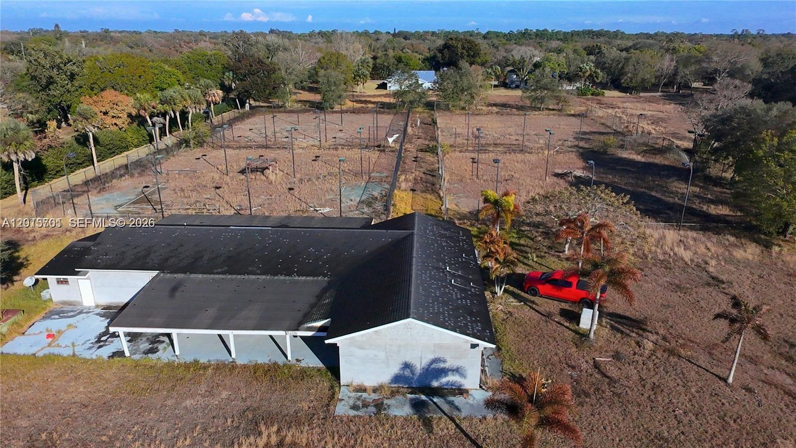 An aerial view shows a building with a dark roof next to fenced tennis courts — 4291 SW 5th Pl SW, Vero Beach FL 32968, VERO BEACH, FL