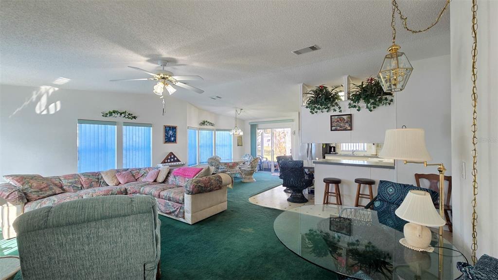 A living room and dining area feature green carpeting, a ceiling fan, and a kitchen bar — 306 BUTTONWOOD COURT, COCOA, FL