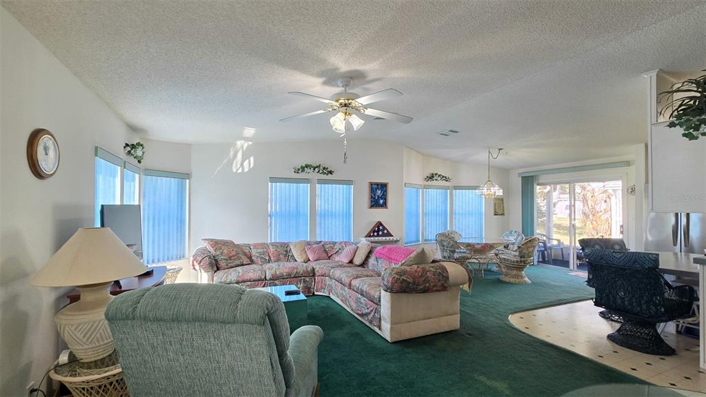 A living room with green carpeting, a sectional sofa, a ceiling fan, and sliding doors — 306 BUTTONWOOD COURT, COCOA, FL
