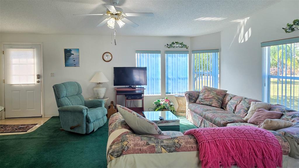 A living room features a green carpet, a patterned sectional sofa, and a teal recliner — 306 BUTTONWOOD COURT, COCOA, FL