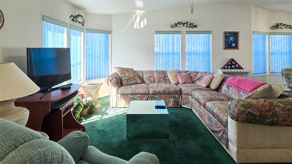 A living room features a large patterned sectional sofa, green carpeting, and multiple windows — 306 BUTTONWOOD COURT, COCOA, FL