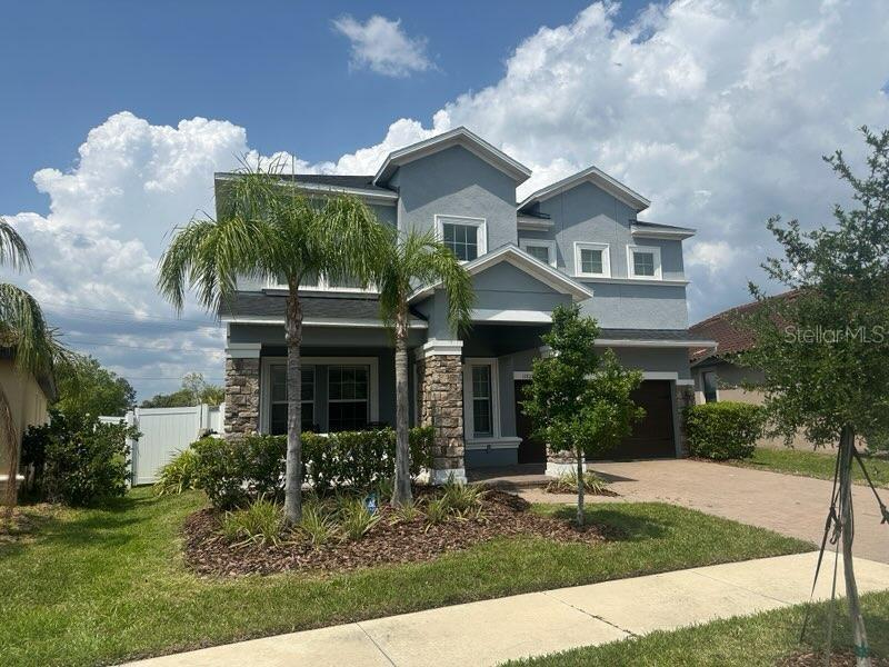 A two-story house with blue siding, stone accents, and a paved driveway under a cloudy sky — 11928 FROST ASTER DRIVE, RIVERVIEW, FL