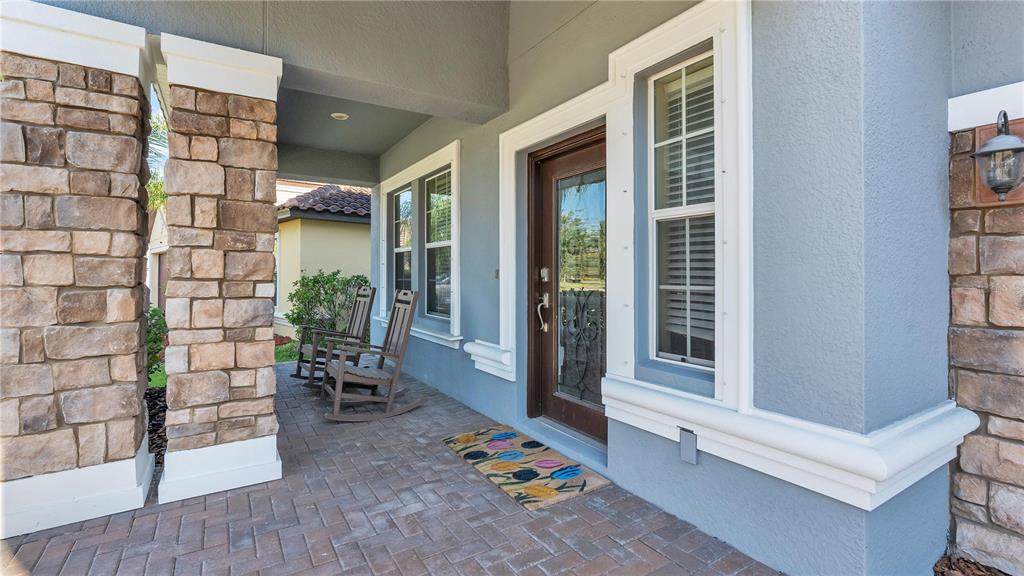 A covered front porch features stone columns, a brick paver floor, and two rocking chairs — 11928 FROST ASTER DRIVE, RIVERVIEW, FL