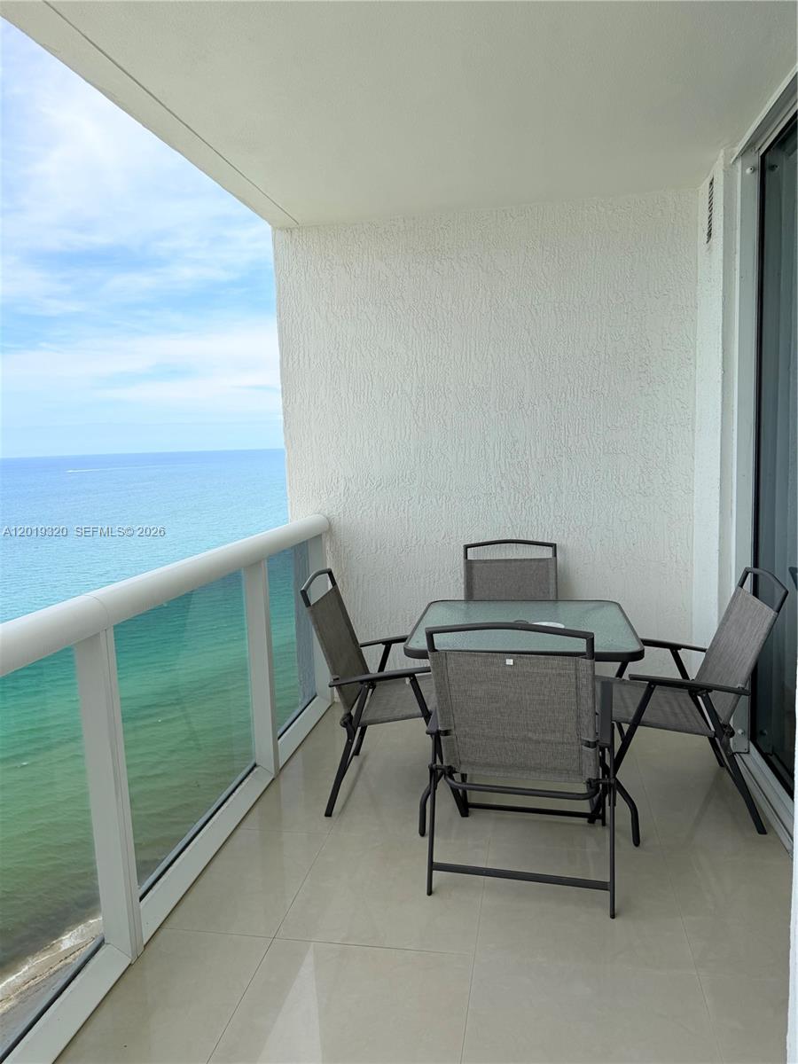 A balcony with a glass-topped table and four chairs overlooks the ocean — 1800 S Ocean Dr # 3002, Hallandale Beach FL 33009, HALLANDALE BEACH, FL