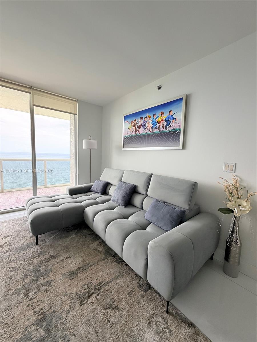 A living room features a grey sectional sofa, a wall painting, and a balcony overlooking water — 1800 S Ocean Dr # 3002, Hallandale Beach FL 33009, HALLANDALE BEACH, FL