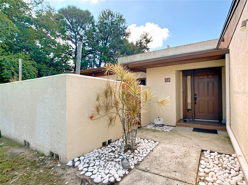 The exterior entrance of a home features a brown door, a privacy wall, and landscaping — 1880 N CRYSTAL LAKE DRIVE UNIT 12, LAKELAND, FL