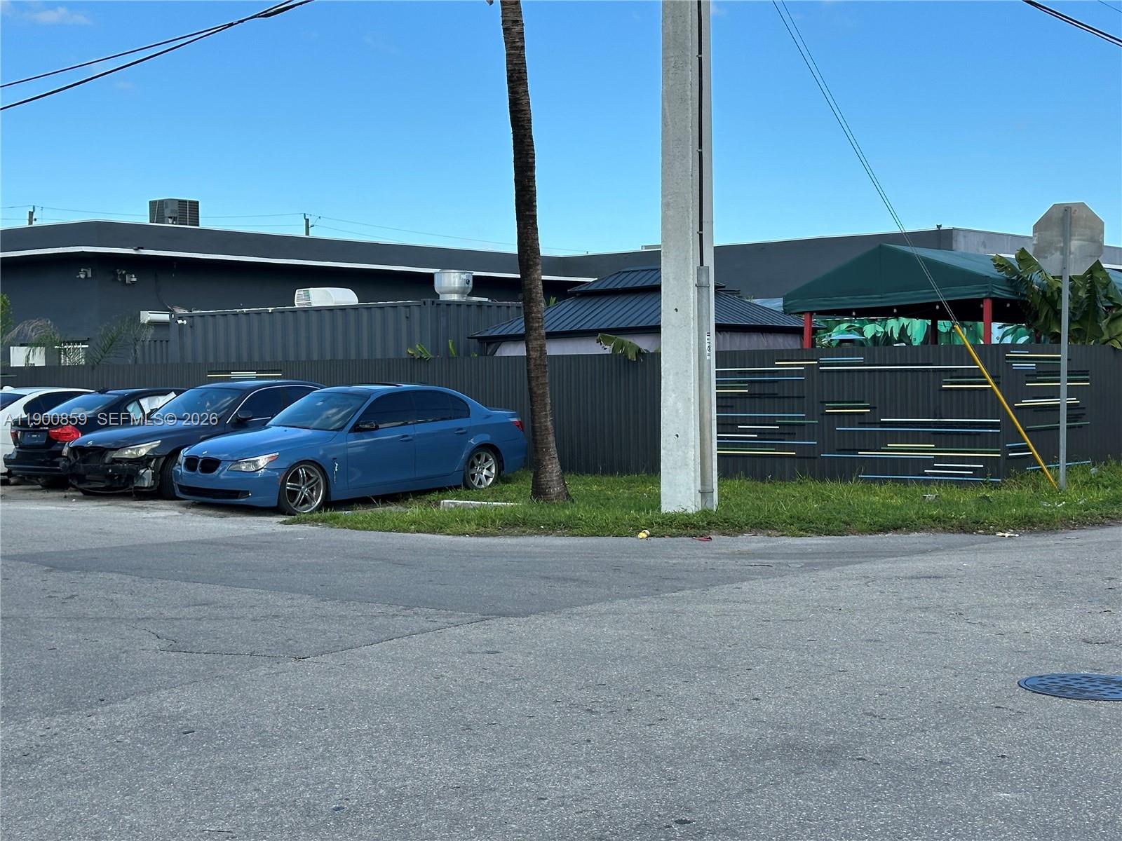 A blue sedan is parked on grass next to a dark fence and a utility pole — 2220 SW 60th Ter, Miramar FL 33023, MIRAMAR, FL