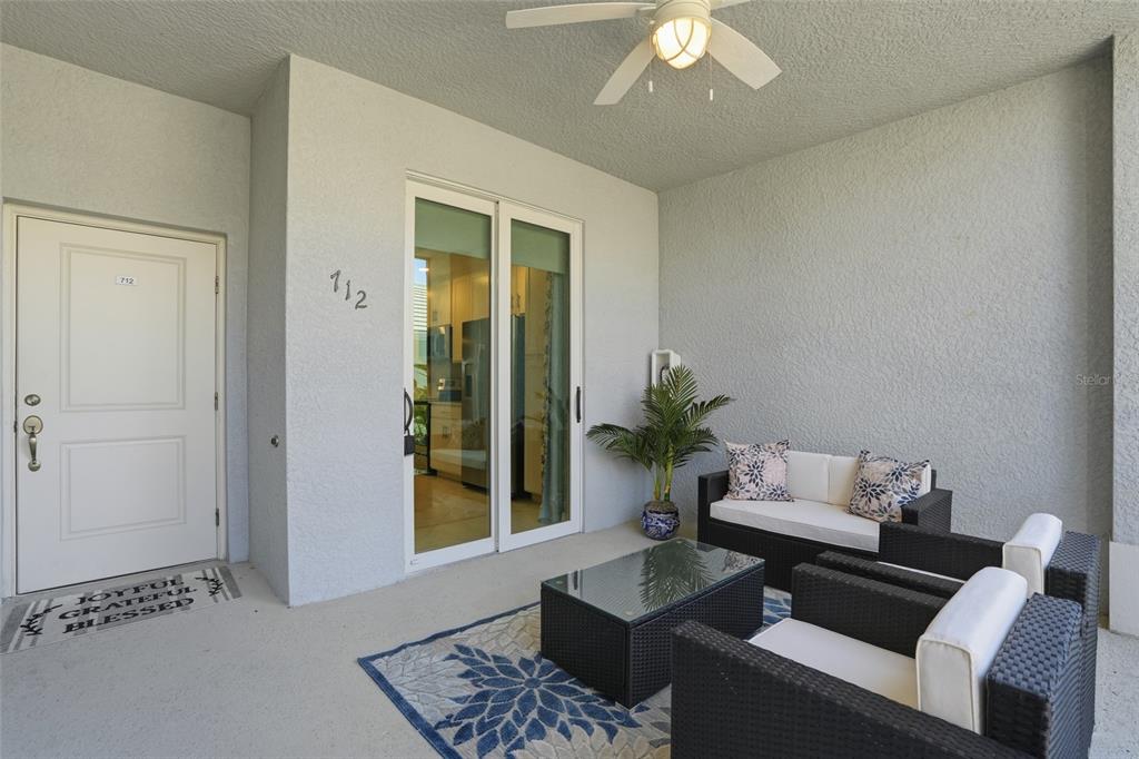 A covered patio features a white door, sliding glass doors, wicker furniture, and a ceiling fan — 14204 HERITAGE LANDING BOULEVARD UNIT 712, PUNTA GORDA, FL
