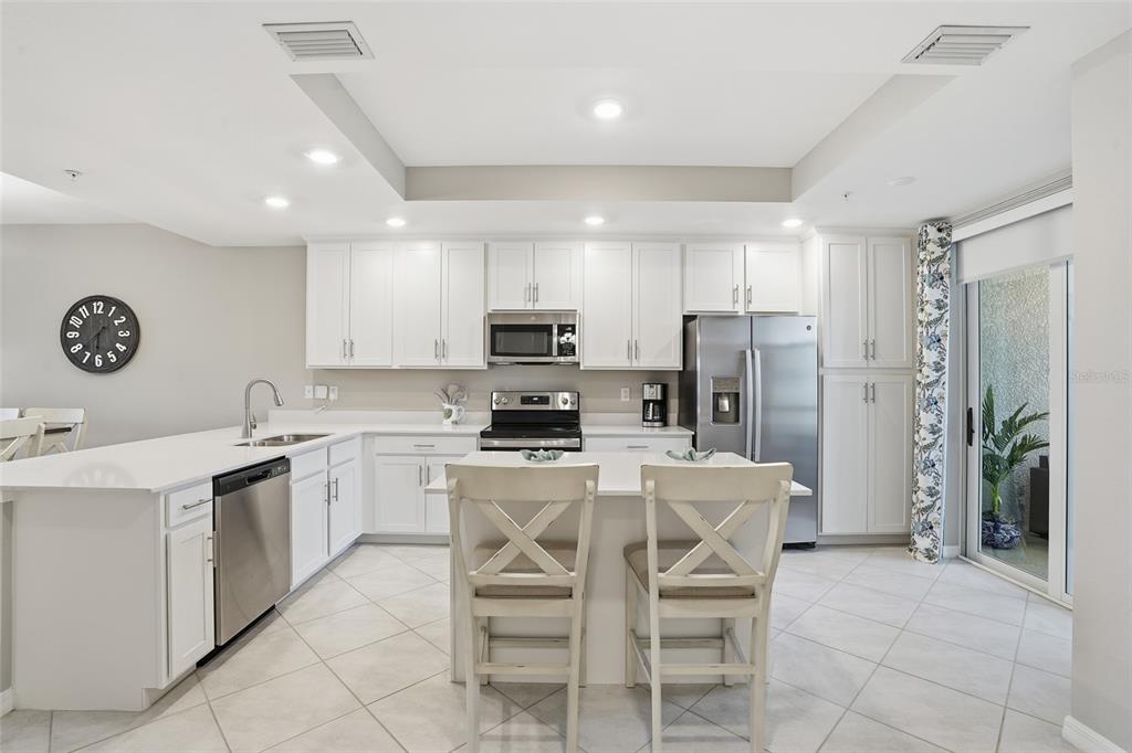 A modern kitchen features white cabinetry, stainless steel appliances, a center island, and tile flooring — 14204 HERITAGE LANDING BOULEVARD UNIT 712, PUNTA GORDA, FL