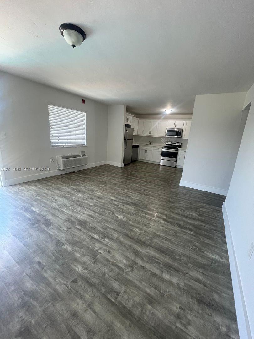 An open-concept living area features wood-look flooring and a kitchen with white cabinetry — 3270 W Trade Ave # 14, Miami FL 33133, MIAMI, FL