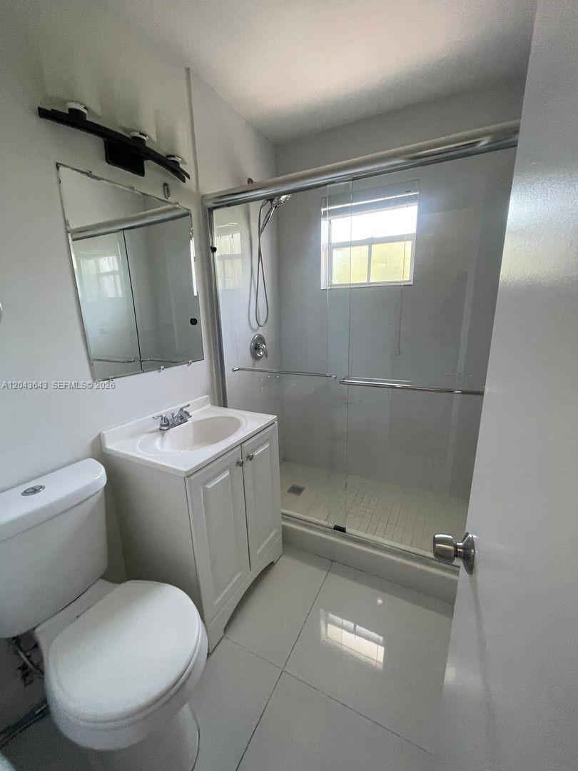 A bathroom features a white vanity, a glass-enclosed shower, and a toilet on tiled floors — 3270 W Trade Ave # 14, Miami FL 33133, MIAMI, FL